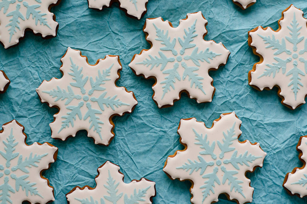 σπιτικά μπισκότα μελόψωμου σε μορφή νιφάδων χιονιού. Επίπεδη σύνθεση με νιφάδες χιονιού και μπισκότα σε μπλε φόντο. - Φωτογραφία, εικόνα
