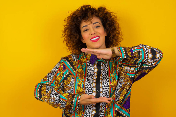 Arab woman wearing colorful shirt  over isolated background gesturing with hands showing big and large size sign, measure symbol. Smiling looking at the camera. Measuring concept. - Photo, Image