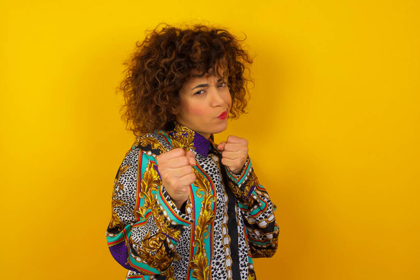 Portrait of attractive  Arab woman wearing colorful shirt with trendy hairstyle and clothes holding hands in front of him in boxing position going to fight. - Valokuva, kuva