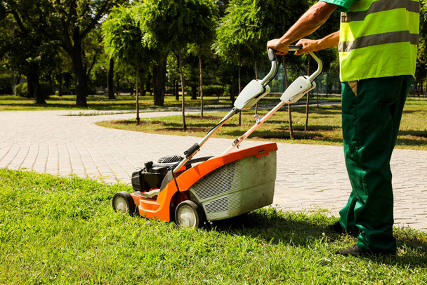 Un travailleur coupe l'herbe avec une tondeuse à gazon dans un parc municipal. - Photo, image