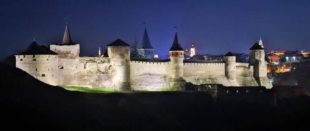 Vista panorámica nocturna del antiguo castillo fortaleza en Kamianets-Podilskyi, región de Khmelnytskyi, Ucrania. Foto del antiguo castillo en una postal o portada. Larga exposición - Foto, imagen