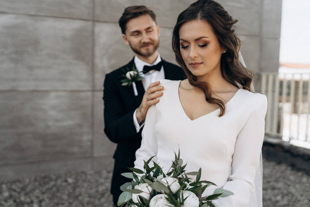 Nevěsta je oblečena v bílých svatebních šatech se svatební kyticí bílých pivoňkových růží a listy eukalyptu v rukou čeká na ženicha. První setkání nevěsty a ženicha - Fotografie, Obrázek