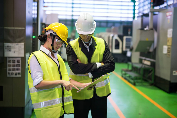 Waist up factory female inspector and her manager discuss inspection report on paper for internal audit at automatic drilling machine. Quality assurance (QA) auditor for manufacturing industry. - Photo, Image