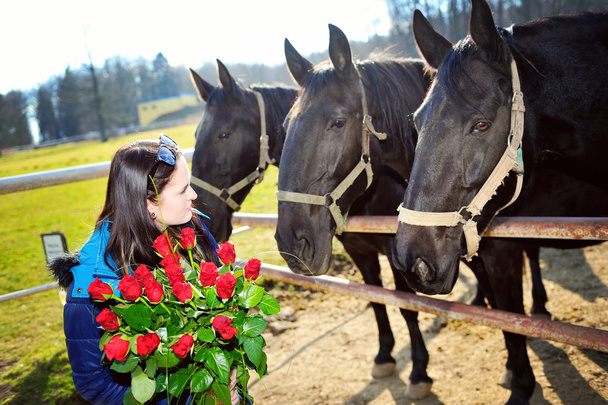 όμορφη νεαρή γυναίκα με μάτσο τριαντάφυλλα και την μαύρα άλογα - Φωτογραφία, εικόνα