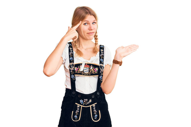 Oktoberfest elbisesi giyen genç ve güzel sarışın kadın avuç içi açık fotokopi alanı ve parmak alnını göstermekten rahatsız oluyor. Bunu bir düşün..  - Fotoğraf, Görsel