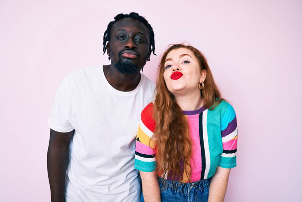 Interracial couple wearing casual clothes looking at the camera blowing a kiss on air being lovely and sexy. love expression.  - Photo, Image