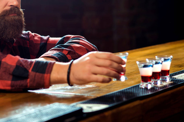 Szakállas férfi alkoholt iszik. Egyedülálló szakállas férfi a pultnál. Alkoholfüggőség. Üveget iszik feles koktéllal.. - Fotó, kép