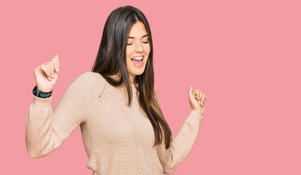 Young brunette woman wearing casual winter sweater dancing happy and cheerful, smiling moving casual and confident listening to music  - Fotoğraf, Görsel