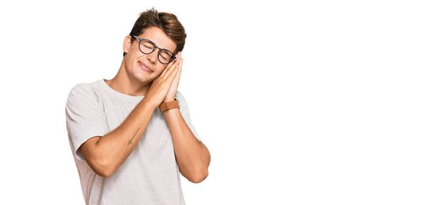 Handsome caucasian man wearing casual clothes and glasses sleeping tired dreaming and posing with hands together while smiling with closed eyes.  - Foto, Bild