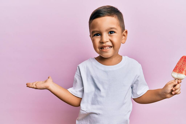 Adorável criança latina segurando sorvete celebrando realização com sorriso feliz e expressão vencedora com mão levantada  - Foto, Imagem