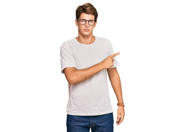 Handsome caucasian man wearing casual clothes and glasses pointing with hand finger to the side showing advertisement, serious and calm face  - Photo, Image