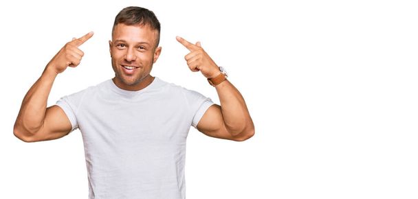 Komea lihaksikas mies päällään rento valkoinen t paita hymyilevä osoittaa päähän molemmin käsin sormella, hyvä idea tai ajatus, hyvä muisti  - Valokuva, kuva