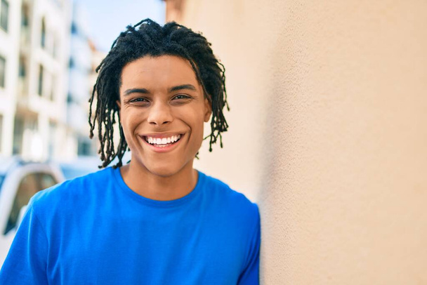 若いアフリカ系アメリカ人の男が笑顔で街の壁に寄りかかって. - 写真・画像