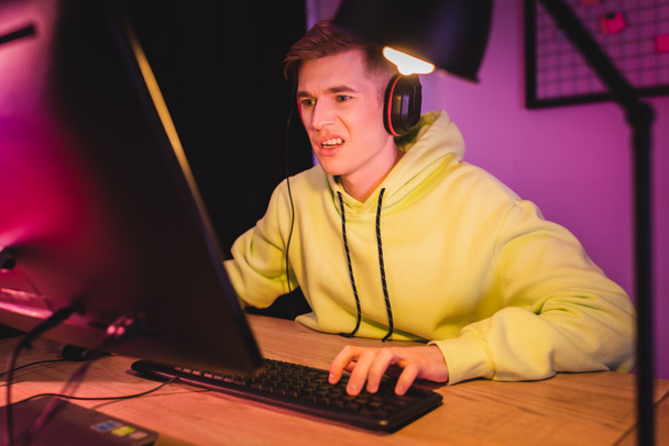 Jugador confuso en auriculares usando computadora en primer plano borroso   - Foto, Imagen