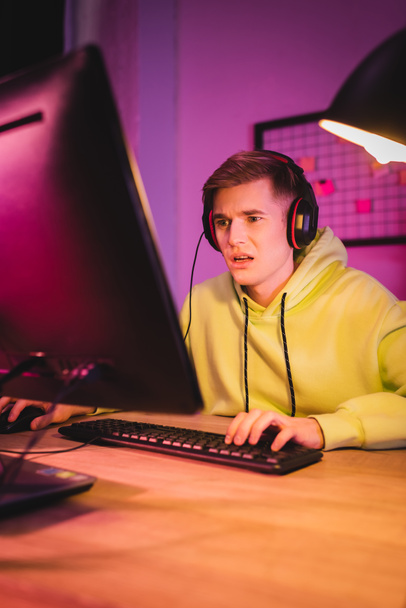 Hombre confundido en auriculares usando la computadora mientras juega videojuego en casa  - Foto, Imagen
