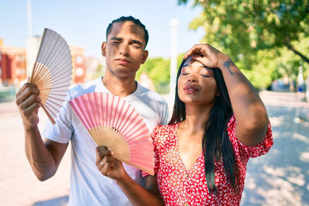 Young latin couple smiling happy using hand fan at street of city. - Photo, Image