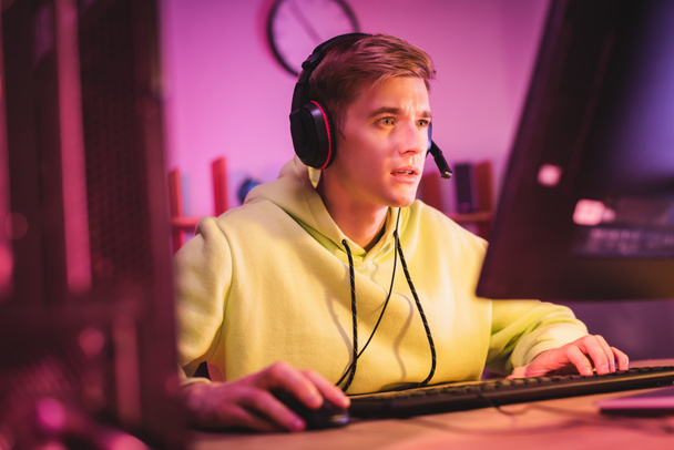 Konzentrierter Gamer im Headset mit Computertastatur und Maus auf verschwommenem Vordergrund  - Foto, Bild