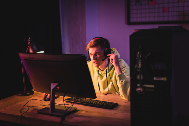 Концентрований геймер в гарнітурі грає на комп'ютері біля лампи на столі
  - Фото, зображення