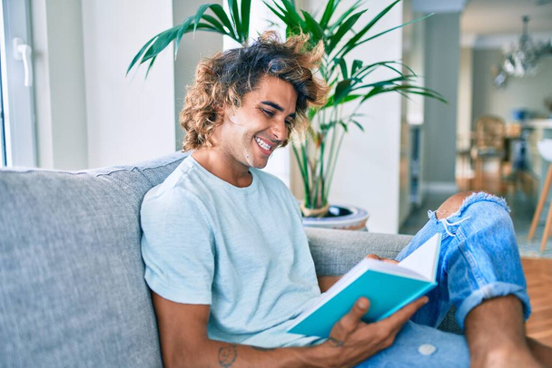Jeune homme hispanique souriant livre de lecture heureux à la maison - Photo, image