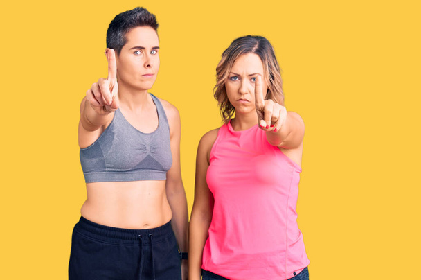 Couple of women wearing sportswear pointing with finger up and angry expression, showing no gesture  - Photo, Image
