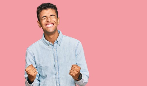 Giovane uomo afroamericano bello indossare abiti casual molto felice ed eccitato facendo gesto vincitore con le braccia alzate, sorridente e urlando per il successo. concetto di celebrazione.  - Foto, immagini