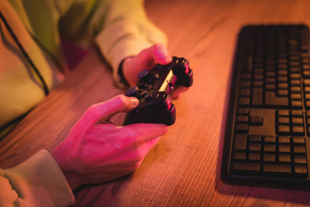 KYIV, UKRAINE - AUGUST 21, 2020: Cropped view of gamer using joystick near computer keyboard on blurred background  - Photo, Image