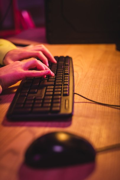 Обрезанный вид геймера с помощью компьютерной клавиатуры рядом с мышью на размытом переднем плане на столе  - Фото, изображение