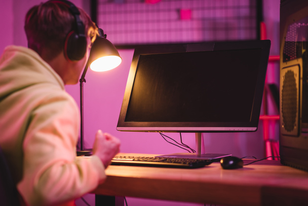 Computer monitor with blank screen near gamer in headset showing yeah gesture on blurred foreground  - 写真・画像