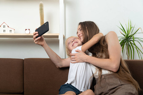 Onnellinen äiti ja poika halaavat ja ottavat selfien älypuhelimella. Kotiin vapaa-aika. - Valokuva, kuva