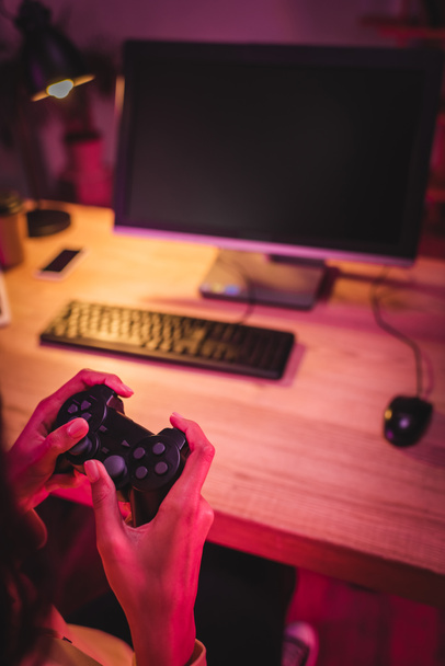 KYIV, UKRAINE - AUGUST 21, 2020: Cropped view of gamer holding joystick near computer on blurred background  - 写真・画像