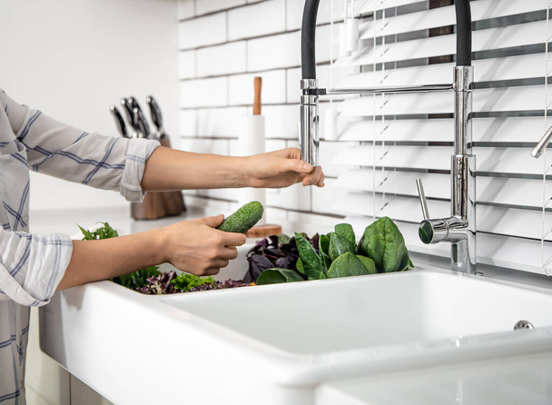 Le mani della donna lavano la lattuga nel lavandino della cucina da vicino. - Foto, immagini