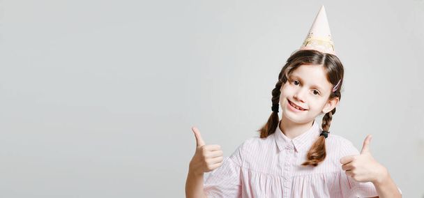 Funny dark-haired girl in a birthday cap in a trendy style. Smiling and fooling around. On a white studio background. Place for an inscription. - Foto, Imagen