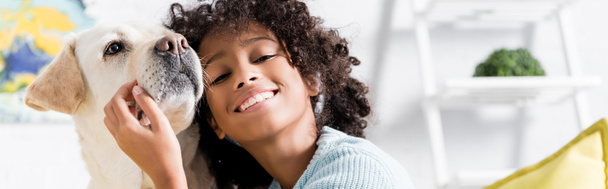 Feliz afroamericana chica apoyada en retriever en casa sobre fondo borroso, pancarta - Foto, Imagen