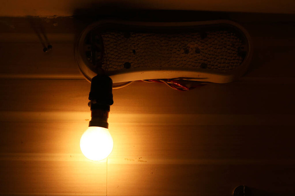 gloeilamp in lampvoet Hangend aan draad op donkere achtergrond - Foto, afbeelding
