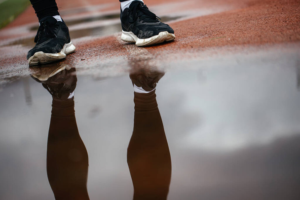 Atletische voeten in sneakers op de loopband. Reflectie van voeten in een plas - Foto, afbeelding
