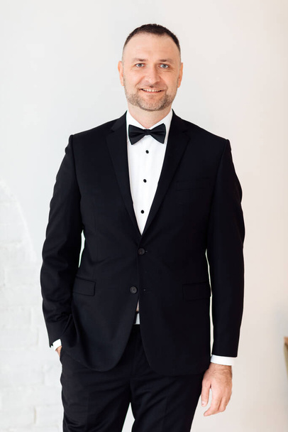 Портрет молодого ділового чоловіка в чорному костюмі і краватці, посміхаючись камері, тримаючи одну руку в кишені на білому тлі. вибірковий фокус
 - Фото, зображення