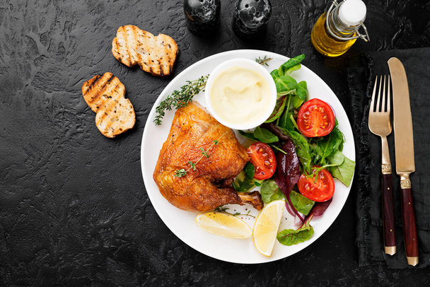 Baked chicken leg, served with sauce and fresh green salad. Black background - Photo, Image