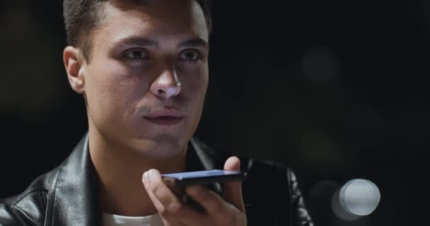 Νεαρός όμορφος άντρας στέλνει φωνητικό μήνυμα τη νύχτα στο πάρκο - Πλάνα, βίντεο