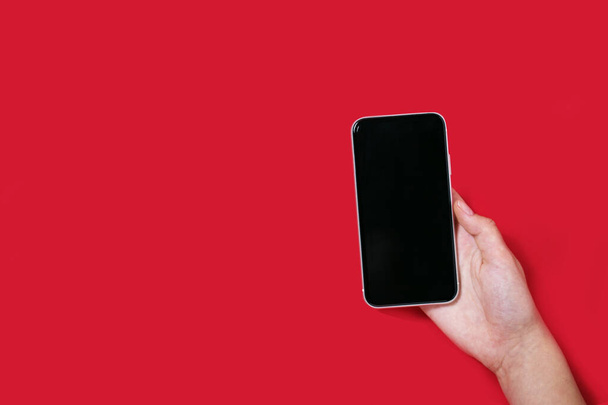Ruka drží telefon na červeném pozadí - Fotografie, Obrázek