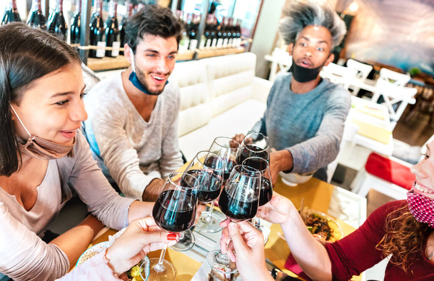 Mensen toasten wijn in restaurant dragen gezichtsmaskers - Nieuwe normale levensstijl concept met vrolijke vrienden plezier samen in wijnmakerij bar - Heldere filter met focus op glazen en gekantelde samenstelling - Foto, afbeelding
