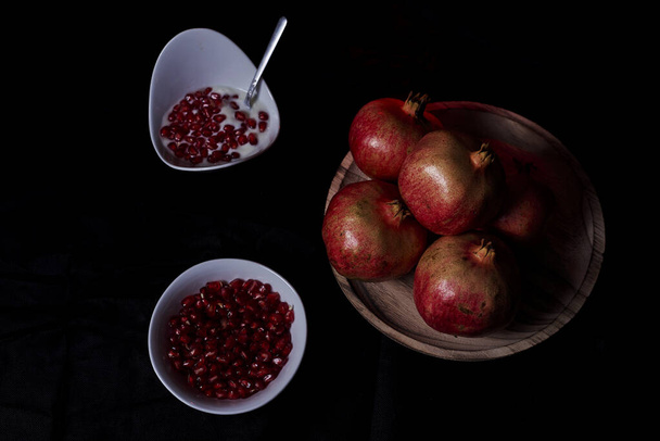 Granadas en mesa y semillas en bol con yogur, Fondo negro, macrofotografía - Foto, imagen