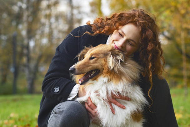 Pretty woman with red hair hugging her collie dog. Female In an autumn park outdoors, cute pet. - Photo, image