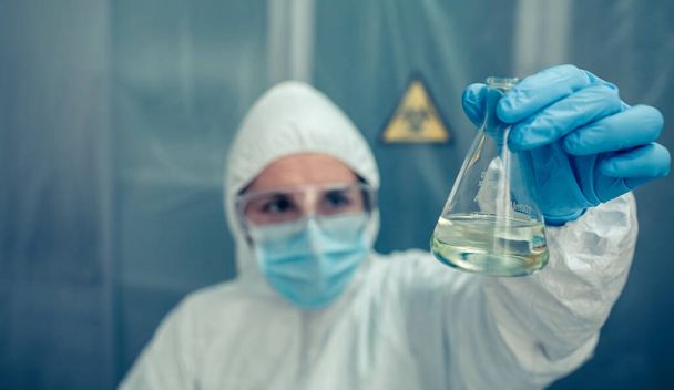 Cientista com terno de proteção olhando tubo de ensaio no laboratório - Foto, Imagem