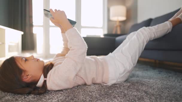 Маленькая девочка с цифровой планшет лежал на спине на полу в уютной комнате - Кадры, видео