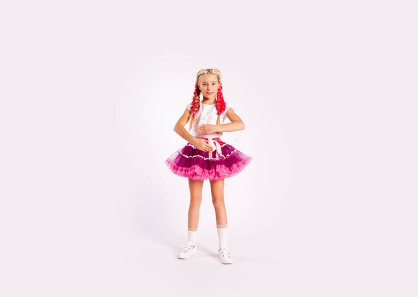 χαριτωμένο κορίτσι σε φωτεινά πολύχρωμα ρούχα και με χρωματιστές πλεξούδες και σε φούστα - Φωτογραφία, εικόνα
