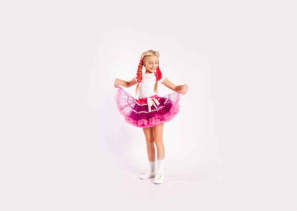 χαριτωμένο κορίτσι σε φωτεινά πολύχρωμα ρούχα και με χρωματιστές πλεξούδες και σε φούστα - Φωτογραφία, εικόνα