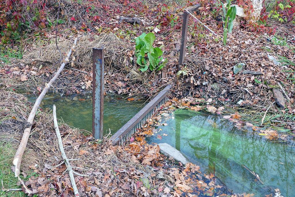ein kleiner Bach mit grünem Wasser und einem eisenbraunen, rostigen Gitter - Foto, Bild