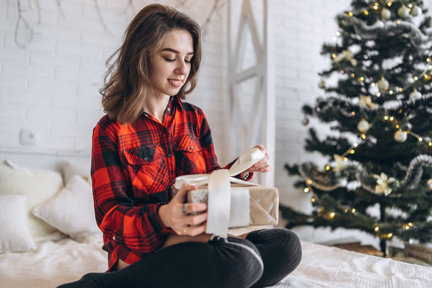 Christmas, New Year. Pretty woman in shirt and socks in bed with christmas gift box, new year tree behin - Fotó, kép