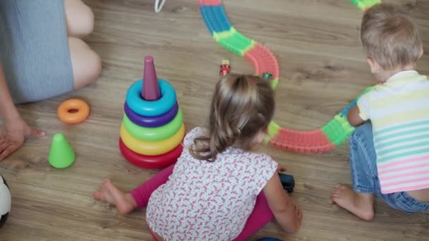 Childhood, games, minor, development concept - top view of mom with newborn baby and children boy and girl sister play with magic road in kid playroom. preschool Siblings have fun at home on quarantine - Footage, Video