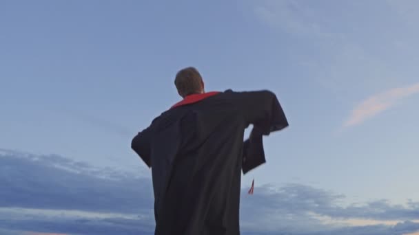 Ένας ευτυχισμένος απόφοιτος με ρόμπα πετάει το καπέλο του - Πλάνα, βίντεο